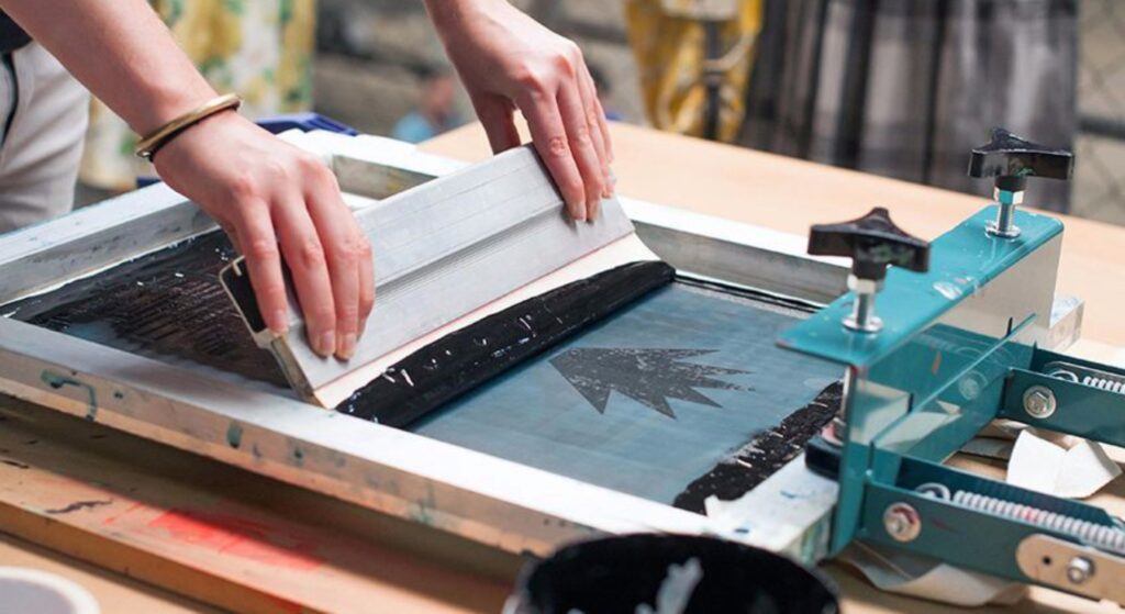 Hands pulling a squeegee across a screen-printing frame